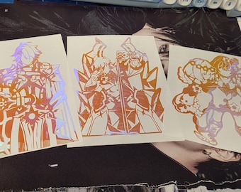 May include: Three holographic stickers featuring anime-style characters. The stickers have orange and iridescent color schemes. The characters are in various action poses, with detailed armor and clothing. The stickers are on a black and white background.