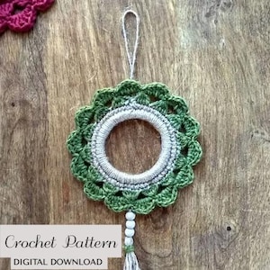 May include: A green and white crocheted wreath with a white tassel hanging from the bottom. The wreath is made of yarn and has a round shape. The wreath is hanging from a string.