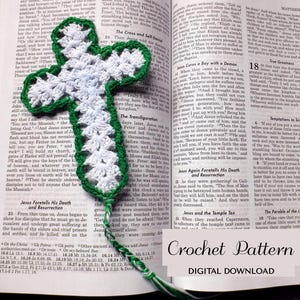 May include: A handmade white and green crochet cross, resting on an open book. The cross is detailed with a white center and green border, and a green cord. The book's pages are visible.