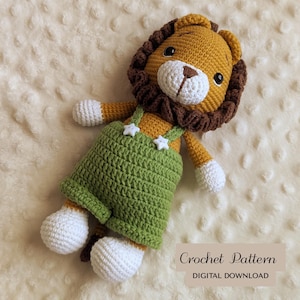 Può includere: Una bambola leone all'uncinetto fatta a mano, con criniera dorata, dettagli marroni e muso bianco. Il leone indossa una tuta verde con bottoni a forma di stella. Il testo "Crochet Pattern DIGITAL DOWNLOAD" è visibile.