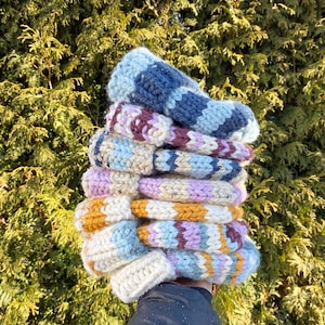 Peut inclure: Une pile de cinq bonnets tricotés colorés dans des tons de bleu, violet, rose, jaune et blanc. Les bonnets sont faits avec un motif en chevron et sont empilés les uns sur les autres.