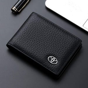 Puede incluir: Cartera de cuero negro con un logotipo de Toyota plateado.