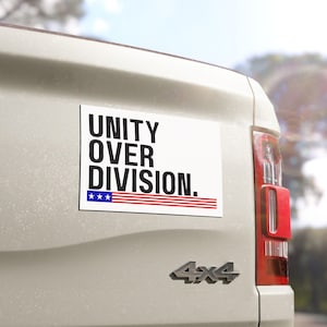 May include: White car with a black and red "Unity Over Division." bumper sticker with a small American flag.
