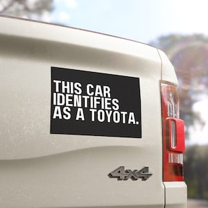 May include: A black and white car sticker with the text "THIS CAR IDENTIFIES AS A TOYOTA." on a white truck.