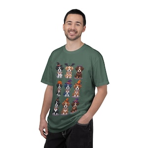 May include: A sage green short-sleeve t-shirt featuring a graphic print of nine cartoon dogs dressed in various Halloween costumes, including witch hats, bat wings, and devil horns, arranged in a three-by-three grid on the front of the shirt.