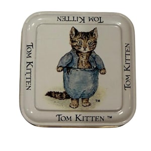 May include: A square, white metal tray featuring a cartoon illustration of Tom Kitten. The image shows a brown and tan kitten wearing a blue outfit. The words "Tom Kitten" are printed around the border of the tray.