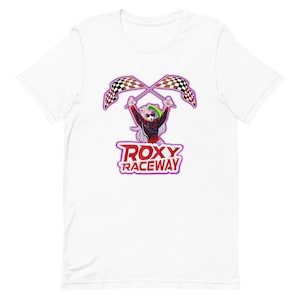Puede incluir: Camiseta blanca con una ilustración de dibujos animados de un personaje peludo sosteniendo banderas a cuadros. El texto "ROXY RACEWAY" está en un contorno morado y rojo.