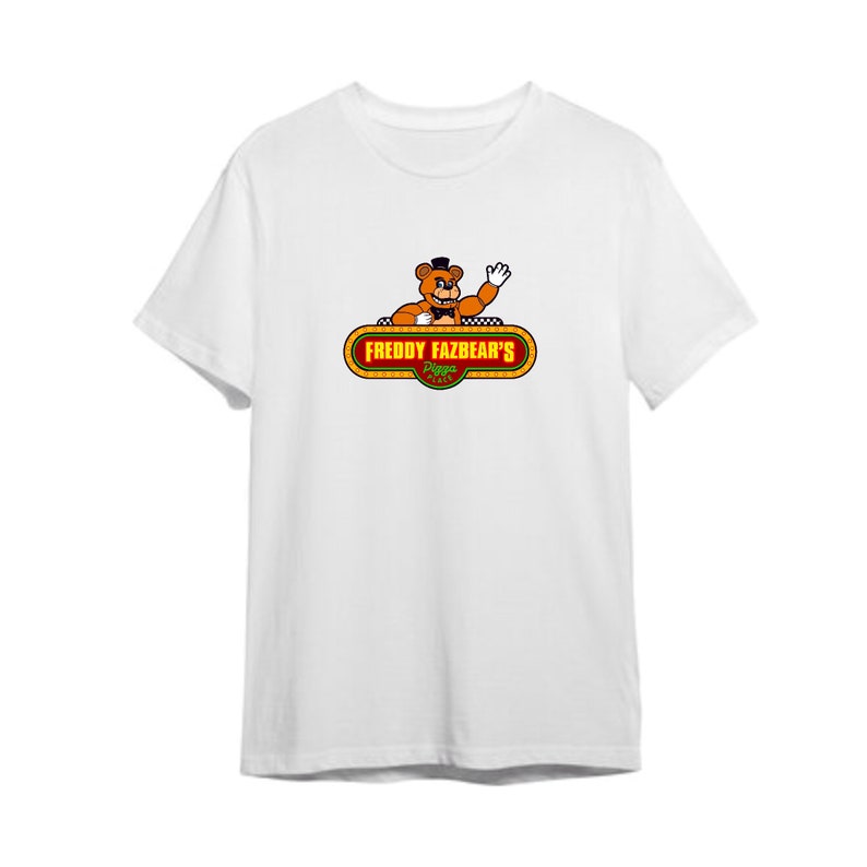 以下が含まれることがあります： フレディ・ファズベアピザのフレディ・ファズベアが描かれた白いTシャツ。グラフィックは、赤い蝶ネクタイと黒いシルクハットをかぶったフレディ・ファズベアが手を振っている漫画です。テキスト「Freddy Fazbear's Pizza」は、赤い縁取りのある黄色のバナーにあります。