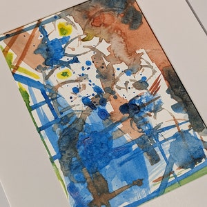 Puede incluir: Pintura abstracta de acuarela en un marco blanco. La pintura presenta una mezcla de colores azules, marrones y amarillos con salpicaduras y pinceladas.
