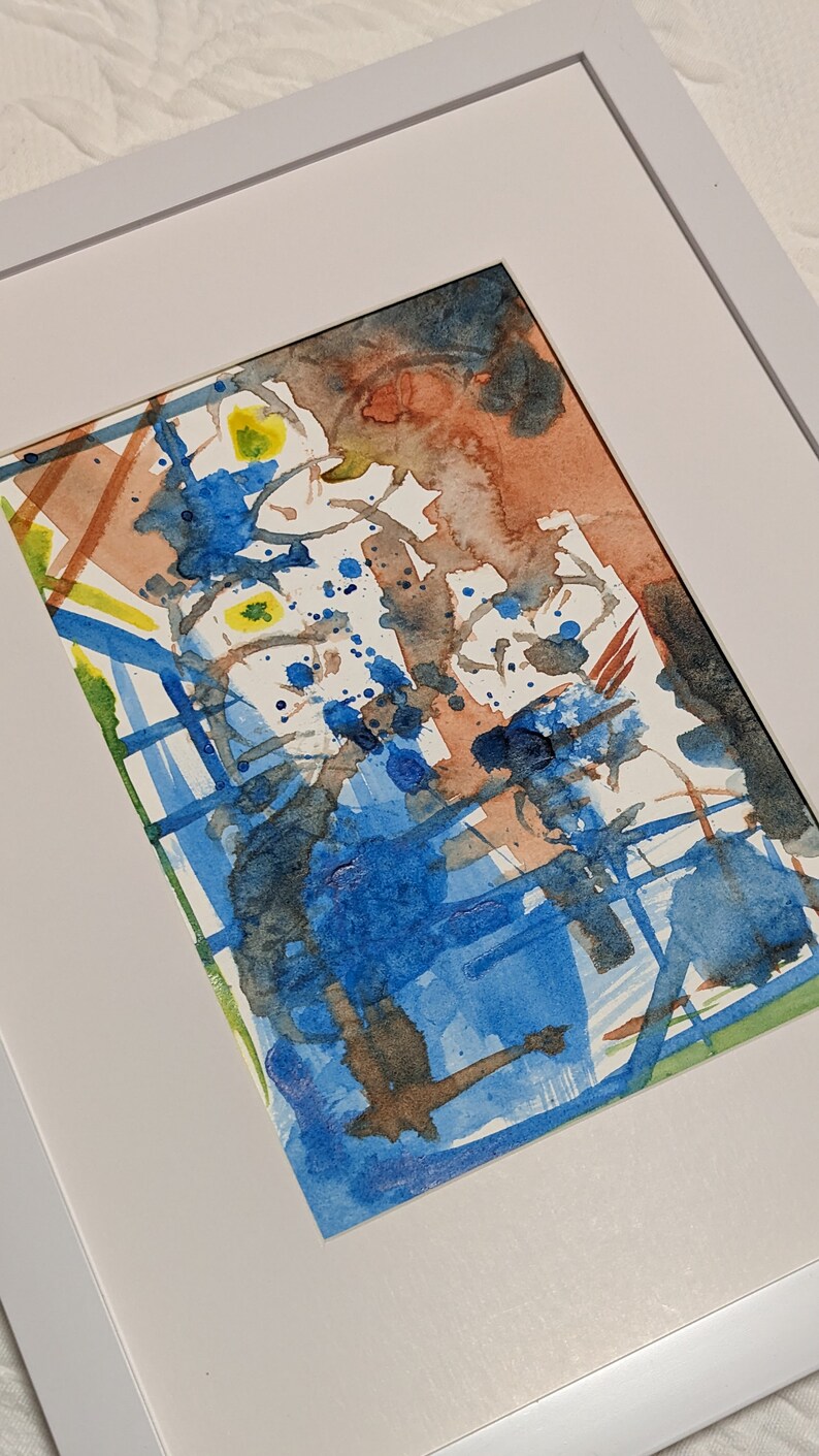 Puede incluir: Pintura abstracta de acuarela en un marco blanco. La pintura presenta una mezcla de colores azules, marrones y amarillos con salpicaduras y pinceladas.