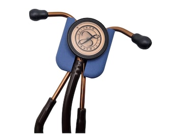 May include: A Littmann stethoscope with a copper finish and a blue rubber earpiece holder. The stethoscope has a black diaphragm with the Littmann logo and the words "Quality" and "Littmann" printed on it.
