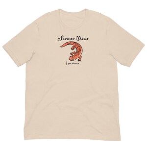 Könnte beinhalten: Ein beiges Kurzarm-T-Shirt mit einer Grafik eines orangefarbenen, gefleckten Molchs. Über dem Molch steht der Text "Former Newt" in einer schwarzen Serifenschrift, darunter steht "I got better." in einer kleineren schwarzen Serifenschrift.