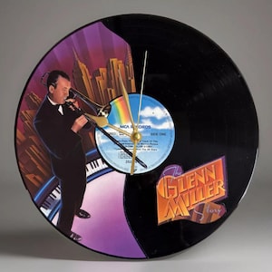 May include: A black vinyl record clock featuring a colorful illustration of a musician playing a trombone, with a cityscape backdrop. The clock face includes the text "The Glenn Miller Story" and "MCA Records". The clock hands are gold.