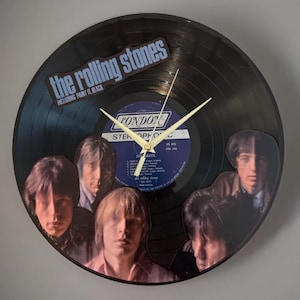 May include: A black vinyl record clock featuring the Rolling Stones logo and band members' images. The clock face includes the text "The Rolling Stones" and "Including Paint It, Black."