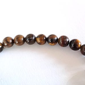 Close-up of a strand of brown and yellow tiger's eye gemstone beads, strung on a thread. The beads are round and smooth, and they center-drilled. They are ideal for necklace, bracelet and earring making.
