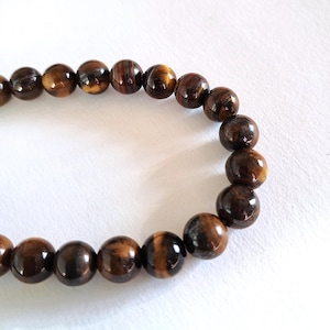 A strand of 8mm natural brown tiger's eye beads, strung on a thread. The beads are round and smooth, and they center-drilled. They are ideal for jewelry making and other crafting projects.