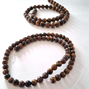Two strands of 6mm and 8mm natural brown tiger's eye beads, strung on a thread. The beads are round and smooth, and they center-drilled. These beads are ideal for necklace, bracelet and earring making and other crafting projects.