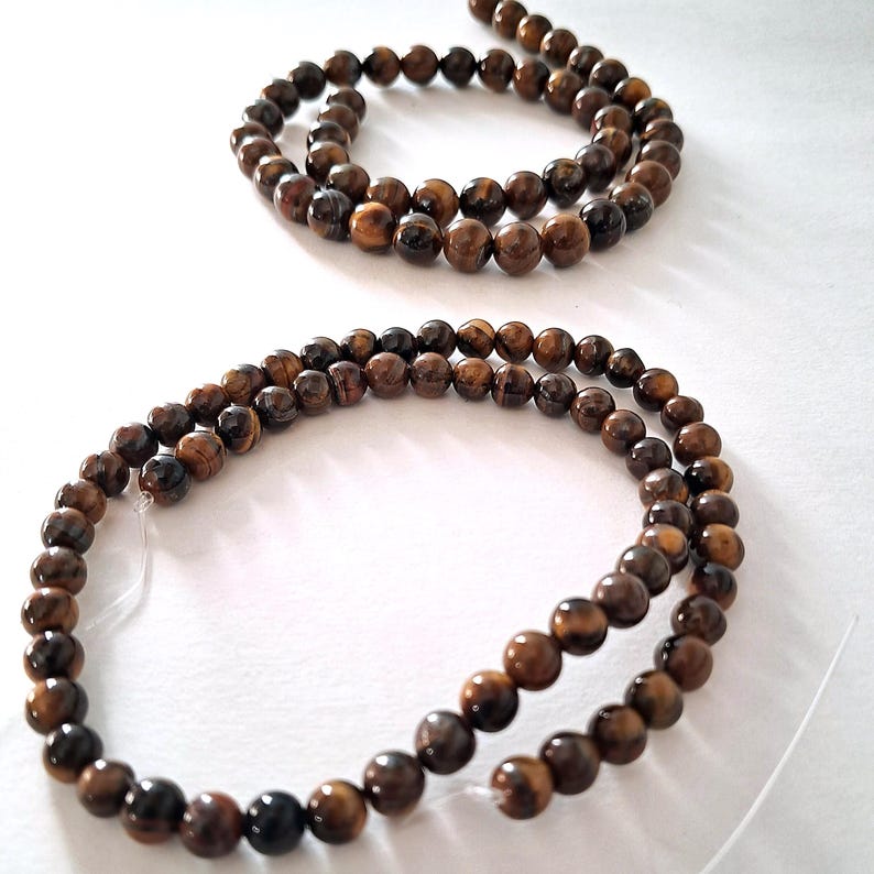 Two strands of 6mm and 8mm natural brown tiger's eye beads, strung on a thread. The beads are round and smooth, and they center-drilled. These beads are ideal for necklace, bracelet and earring making and other crafting projects.