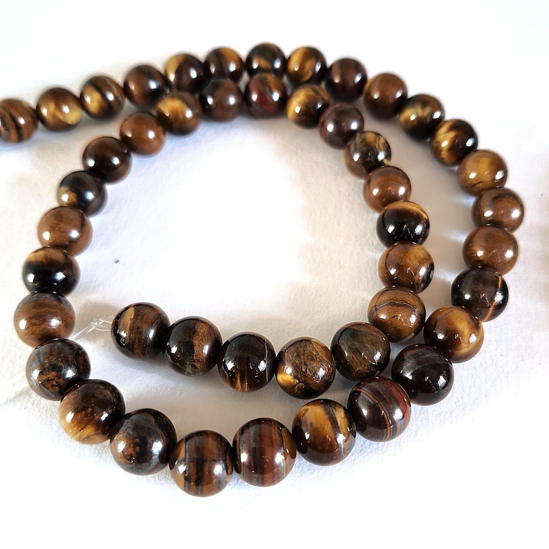 A strand of natural brown tiger's eye beads, strung on a thread. The beads are round and smooth, and they are center-drilled. They are ideal for necklace, bracelet and earring making.