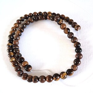 A strand of natural brown tiger's eye beads, strung on a thread. The beads are round and smooth, and they center-drilled. They are ideal for jewelry making and other crafting projects.