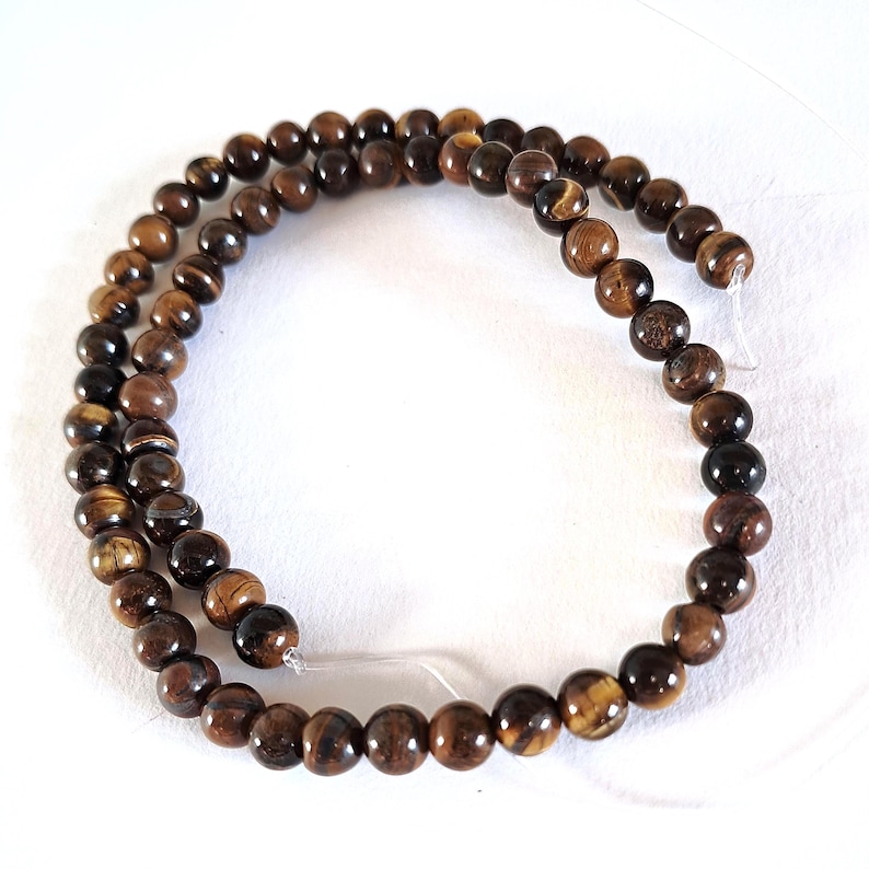 A strand of natural brown tiger's eye beads, strung on a thread. The beads are round and smooth, and they center-drilled. They are ideal for jewelry making and other crafting projects.