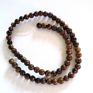 A strand of brown tiger's eye beads, strung on a thread. The beads are round and smooth, and they center-drilled. They are ideal for making beaded necklaces, bracelets and earrings.