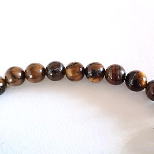 A strand of natural yellow-brown tiger's eye beads, strung on a thread. The beads are round and smooth, and they center-drilled. These beading supplies are ideal for necklace, bracelet and earring making.