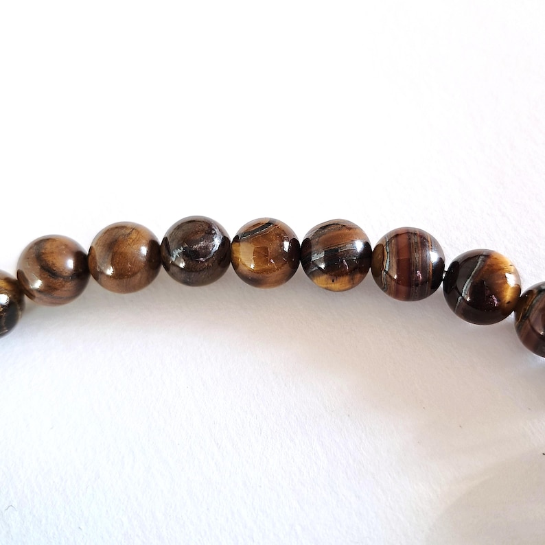 A strand of natural yellow-brown tiger's eye beads, strung on a thread. The beads are round and smooth, and they center-drilled. These beading supplies are ideal for necklace, bracelet and earring making.