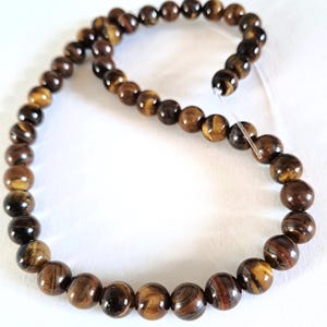A strand of natural brown tiger's eye gemstone beads, strung on a thread. The beads are round and smooth, and they center-drilled. They are essential beading supplies.