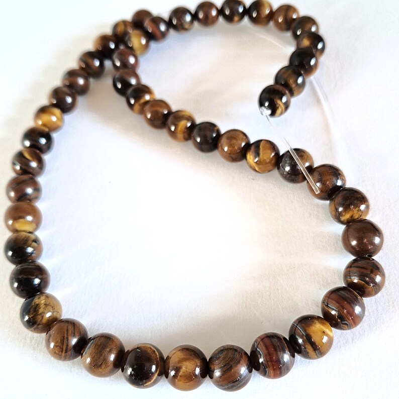 A strand of natural brown tiger's eye gemstone beads, strung on a thread. The beads are round and smooth, and they center-drilled. They are essential beading supplies.