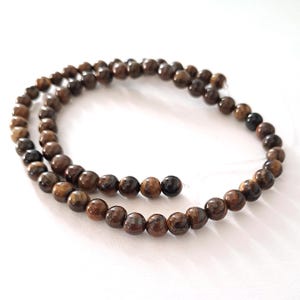 A strand of brown tiger's eye gemstone beads, strung on a thread. The beads are round and smooth, and they are center-drilled. They are ideal for necklace, bracelet and earring making.
