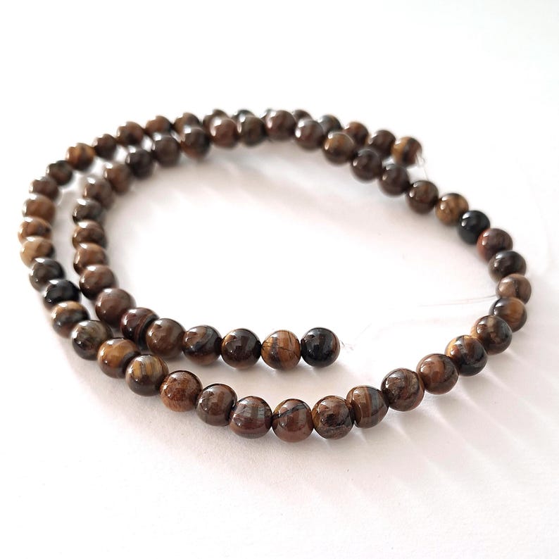 A strand of brown tiger's eye gemstone beads, strung on a thread. The beads are round and smooth, and they are center-drilled. They are ideal for necklace, bracelet and earring making.