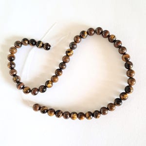A strand of 6mm natural brown tiger's eye beads, strung on a thread. The beads are round and smooth, and they center-drilled. They are ideal for making beaded necklaces, bracelets and earrings.
