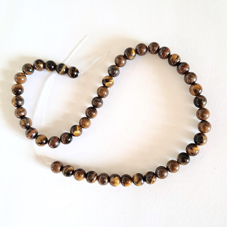 A strand of 6mm natural brown tiger's eye beads, strung on a thread. The beads are round and smooth, and they center-drilled. They are ideal for making beaded necklaces, bracelets and earrings.
