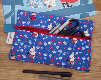 May include: Blue pencil case with a red zipper, filled with pens, scissors, and other supplies. The case features a pattern of white flowers and cartoon characters. A matching blue folder with cartoon illustrations is in the background.