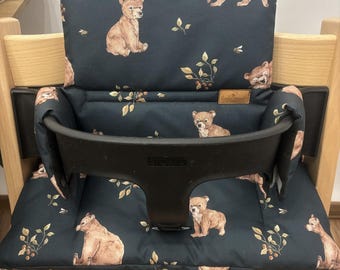May include: A dark blue high chair cushion with a bear print. The cushion has a black strap and a brown label that says "Little Dutch".