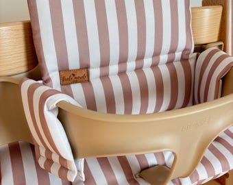 May include: A high chair cushion set featuring a vertical striped pattern in dusty rose and white. The padded fabric covers the backrest and seat, with a brown leather-like tag labeled trele morele shop attached to the backrest cushion.