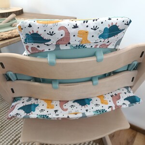 May include: A light blue high chair with a white and blue dinosaur print cushion and a white and yellow dinosaur print back cushion.
