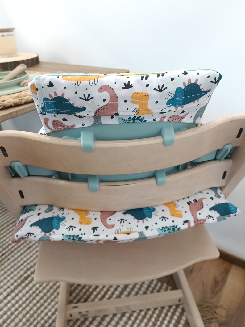 May include: A light blue high chair with a white and blue dinosaur print cushion and a white and yellow dinosaur print back cushion.