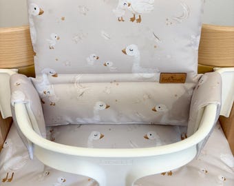 May include: A white high chair with a gray and white goose-themed cushion. The cushion has a white border and a small brown label that says "Little Goose".