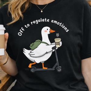 Puede incluir: Una taza de cerámica blanca con un asa negra y el texto "But First, Coffee" en negrita negra. La taza se encuentra sobre un fondo neutro, resaltando su diseño simple.