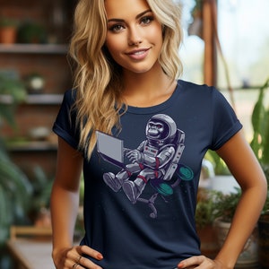May include: A navy blue t-shirt with a graphic of a monkey astronaut sitting in a chair and using a laptop. The monkey is wearing a white helmet and has red eyes.