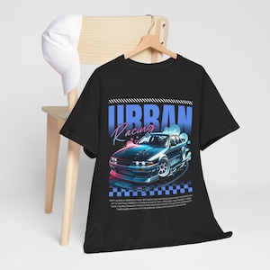 May include: Black t-shirt with a blue and pink graphic of a car drifting with the text "Urban Racing" above it. The text below the car reads "Drift legend, a term reserved for those rare individuals who have mastered the art of drifting. Embodies a unique blend of skill, precision, and passion. These are the ones who push the limits of physics and innovation within the drifting community. Their names spoken with reverence among enthusiasts worldwide."