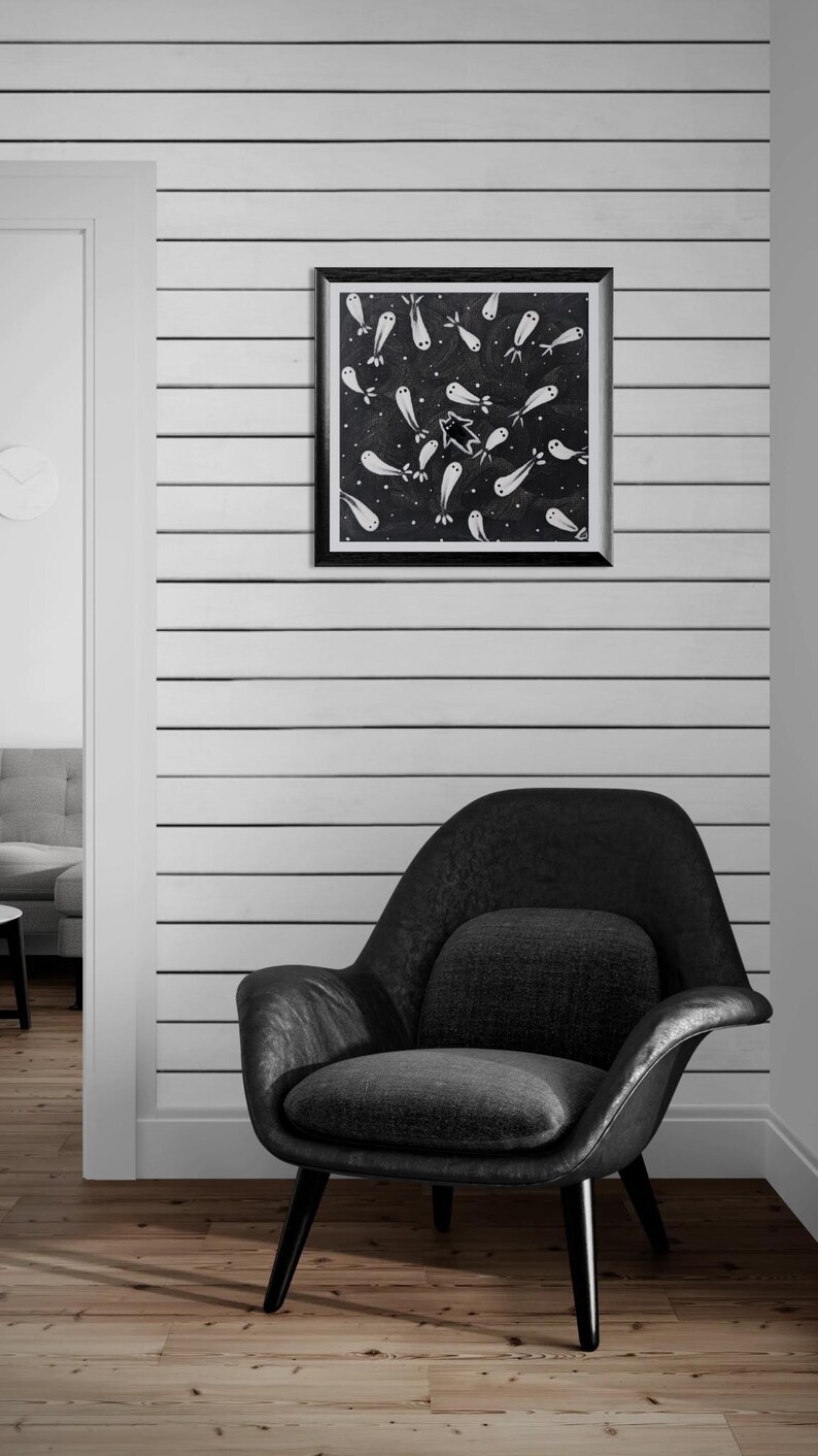 May include: A black and white framed artwork featuring a pattern of ghost-like figures on a dark background hangs above a black armchair. The wall is white with horizontal black stripes. The room has wooden flooring.