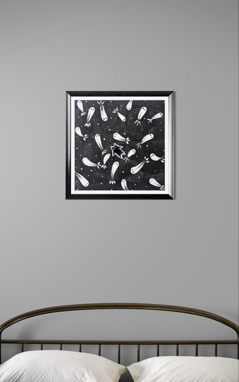 May include: A framed artwork featuring a black background with white, ghost-like figures and a star. The figures are scattered across the canvas, creating a whimsical and slightly spooky design. The frame is black.