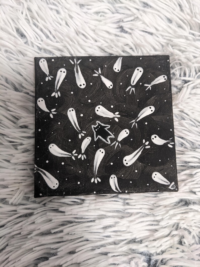 May include: Square canvas art featuring a black background with white dots and whimsical white ghost-like figures. A black cat silhouette is also present. The artwork has a playful, spooky theme, perfect for Halloween or adding a touch of whimsy to any space.