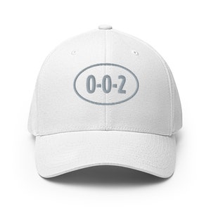 Peut inclure: Casquette de baseball blanche avec un patch ovale gris brodé sur le devant, qui dit "0-0-2".