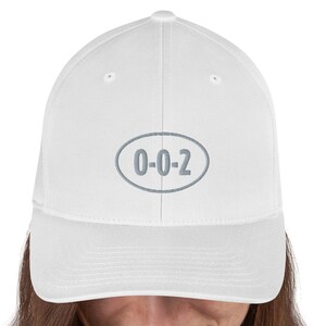 以下が含まれることがあります： 前面に「0-0-2」と刺繍されたグレーの楕円形のワッペンが付いた白い野球帽