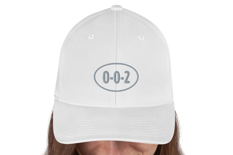 以下が含まれることがあります： 前面に「0-0-2」と刺繍されたグレーの楕円形のワッペンが付いた白い野球帽