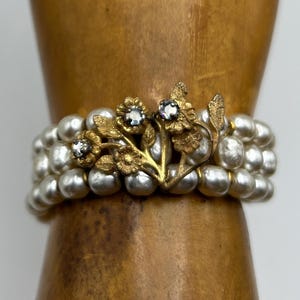 May include: A gold and silver bracelet with a floral design and clear stones. The bracelet is made of pearls and has a delicate, feminine look.
